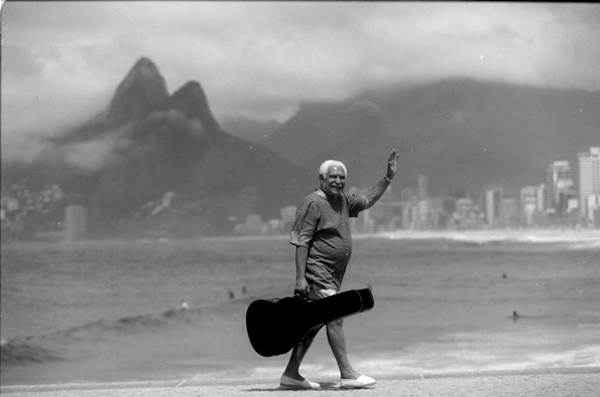 Imagem do msico Dorival Caymmi, com case de violo, caminhando na orla da praia, exibida na exposio Caymmi 100 anos, em cartaz no Museu dos Correios (Arquivo Pessoal)